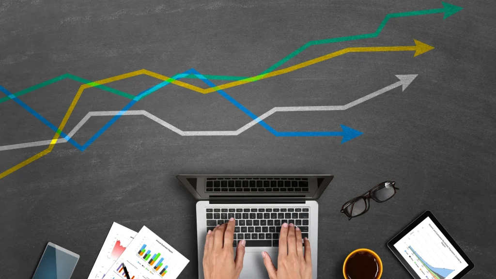 Hands typing on a laptop surrounded by market research graphs, analyzing data for digital marketing strategies.