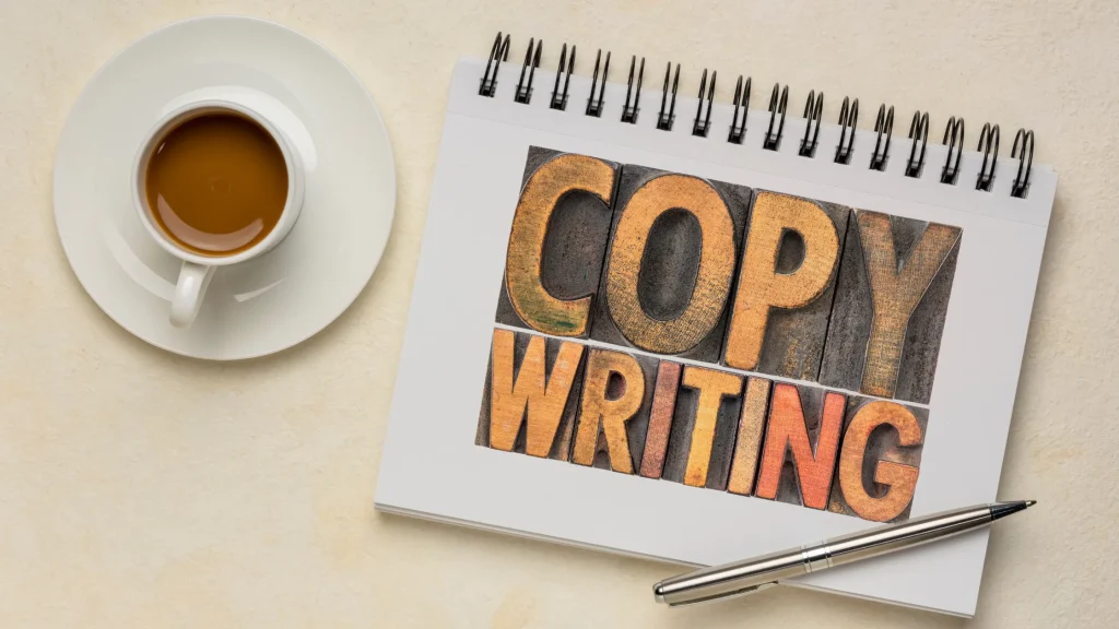 A coffee cup and a notebook with the words "COPYWRITING" in large, wooden letter blocks.